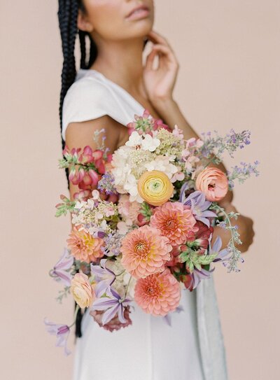 Black bride with long braids holding a colorful bouquet