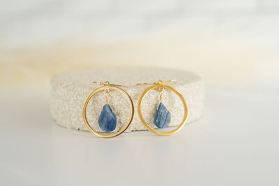 handmade earrings with natural stone in the middle of gold circles sitting upright against a stone ledge