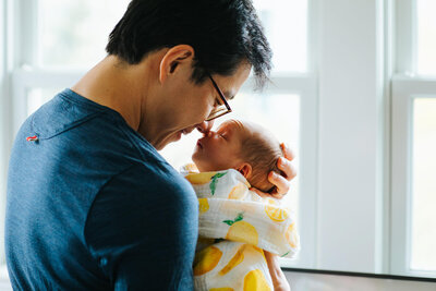 New dad holding infant son in a Somerville MA nursery, photographed by Boston newborn photographer AM Family Photography