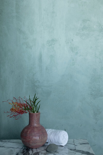 Bathroom plaster render wall in green with pink handmade ceramic vase with grevillea flower and linen towel on marble top