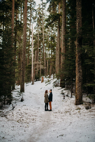lgbt couple stand in a snowy path with trees on either side in Mount Hood, Oregon