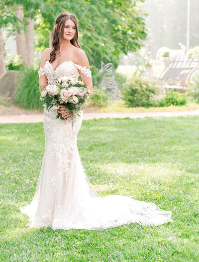 A smiling brunette bride holding her wedding bouquet in a Raleigh park by JoLynn Photography, a Raleigh wedding photographer