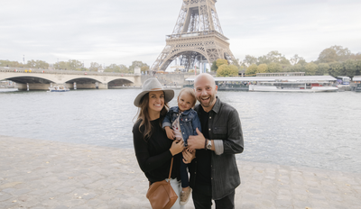 The Benfield family in Paris France smiling in front of the eiffel tower with two year old daughter, Scout
