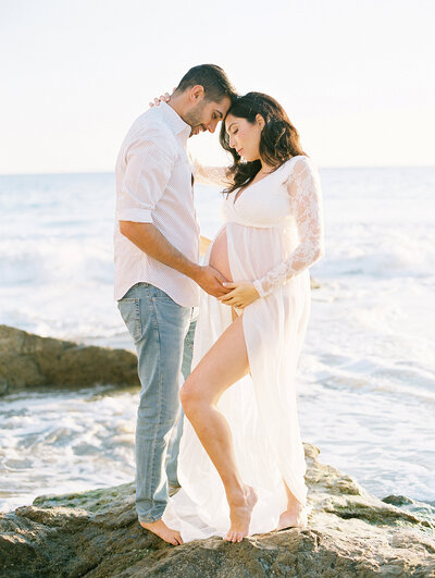 A couple looking at mom's belly during  beach maternity portraits by photographer Daniele Rose