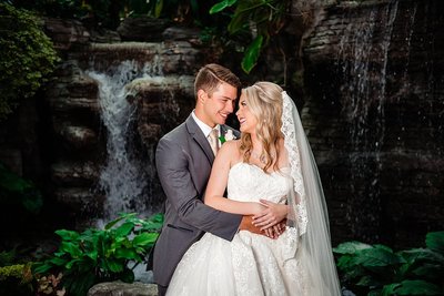 Bride and groom smiling at one another on their wedding day with a waterfall behind them