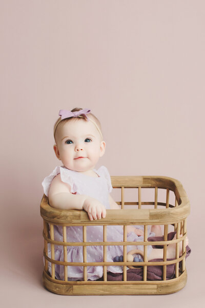 6 month old baby sitting in a crate on a purple backdrop