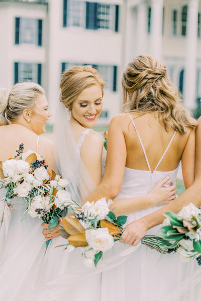 bride looks over her shoulder while embracing her bridesmaids