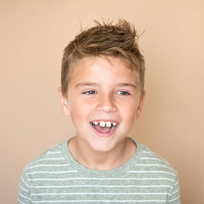 young boy being silly wearing a sage and white striped shirt in front of a tan background