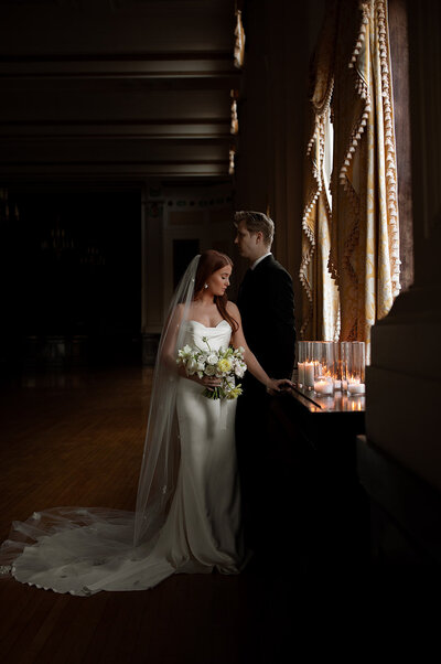 Bride & Groom standing near window with bouquet