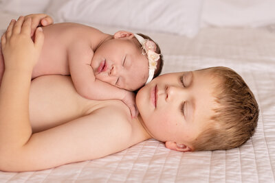 A small boy laying on a bed with a newborn baby laying on top of him.