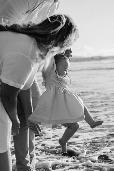 A little family on the beach swinging their child in the air while photographed by taranaki wedding photographer aimee kelly photography