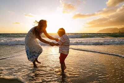 A mother holds the hands of her son as they splash and play along the water.