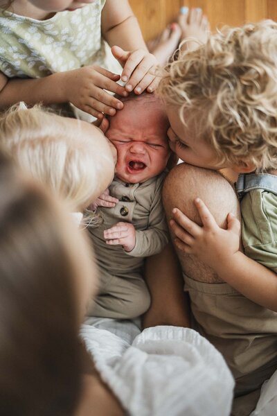 Siblings kissing new baby brother