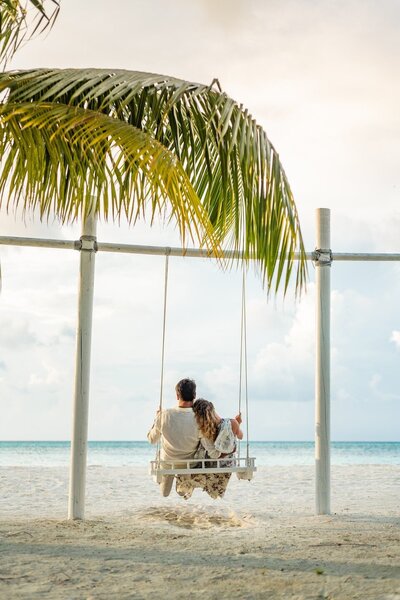 Couple on swing under palm tree on beach