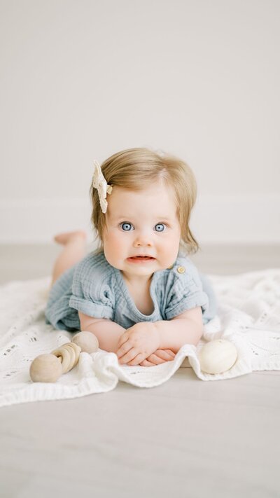 Baby girl with big blue eyes lays on knit blanket during baby studio photography session