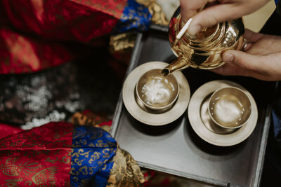 groom pouring korean alcohol from a gold teapot into a brass cup on a wooden tray