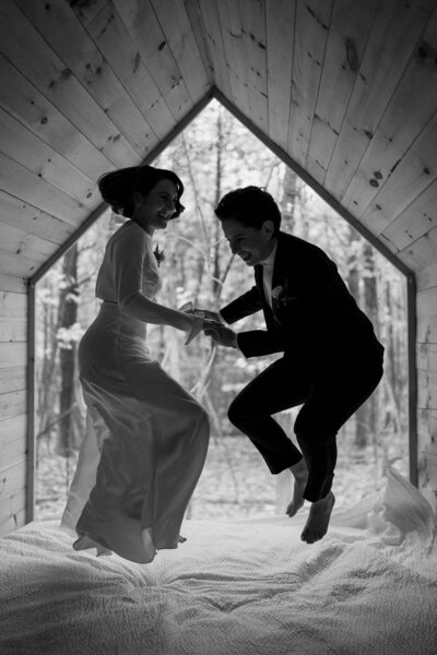 Black and white photo of a bride and groom jumping inside a cabin