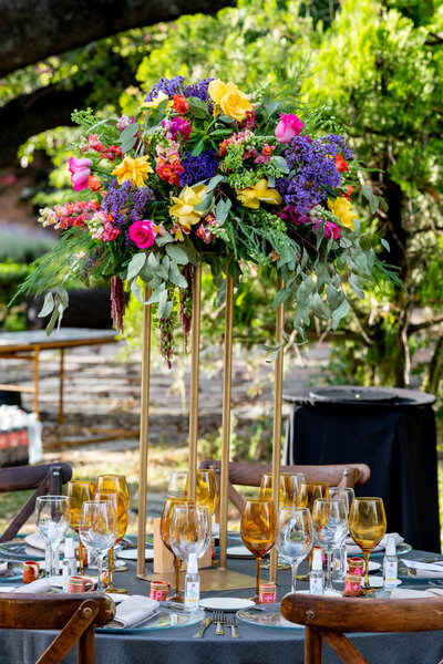 A colorful flower centerpiece surrounded by glasses, plates and utensils on top of the table
