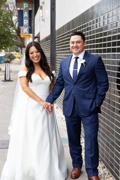 An Austin-based wedding photographer captures the intimate moment of a bride and groom holding hands on the sidewalk.
