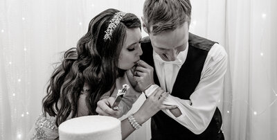 Playful and intimate moment of a bride licking frosting from the groom’s finger during their wedding cake cutting at a Colorado reception.