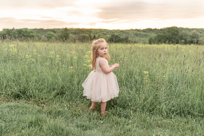 Little girl standing at edge of field at sunset in pink dress