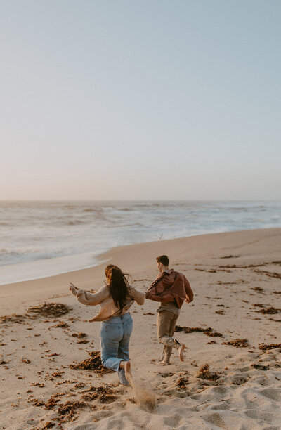 couple runs on the beach during an engagement session at half moon bay california