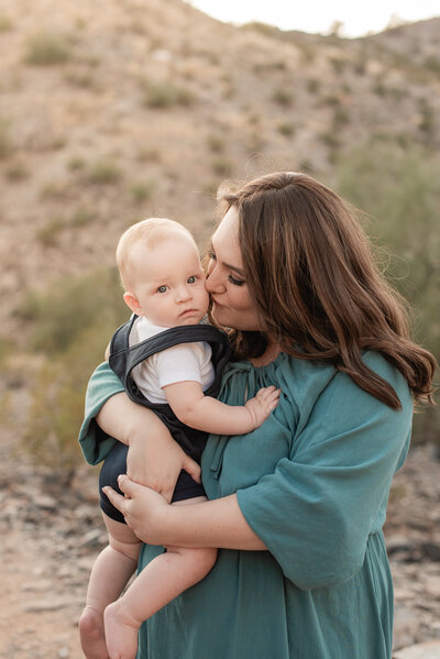mom in a green dress snuggles her 1 year old among the Phoenix desert mountain
