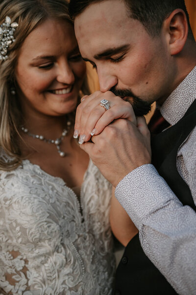 Groom kisses bride's hand, showing her engagement ring as they smile in wedding attire—capturing real moments during their Colorado wedding day.