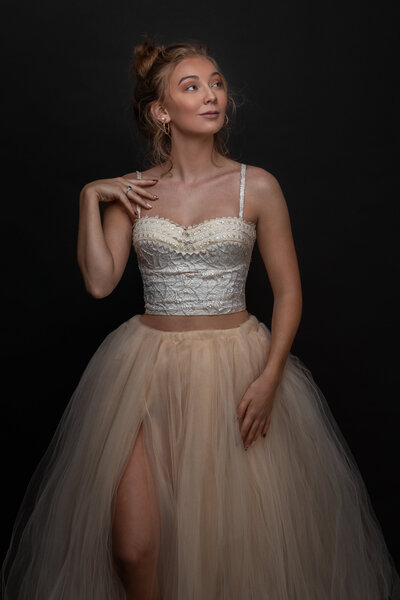 woman in tulle dress looking sideways with right hand on shoulder and left hand on dress