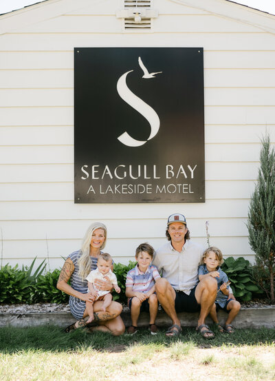 the owners of Seagull Bay Motel sit on the lawn in front of the motel sign with their three young sons