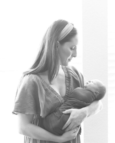 mother with newborn baby next to a window in soft black and whit