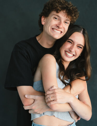 Close up image of couple with their arms around each other on a dark studio background