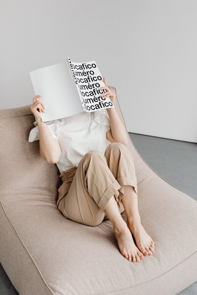 Minimally stylish woman laid back holding up a magazine to read with a monochrome typographic striking cover.