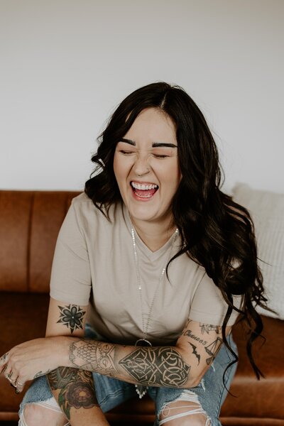 Photographer with tattoos laughing while sitting on a leather couch