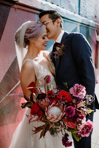Fun and colorful bride and groom kiss on their wedding day with large bohemian bouquet