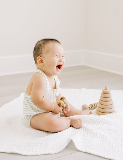 Baby boy in striped romper plays with wooden toys during baby photo session in Raleigh