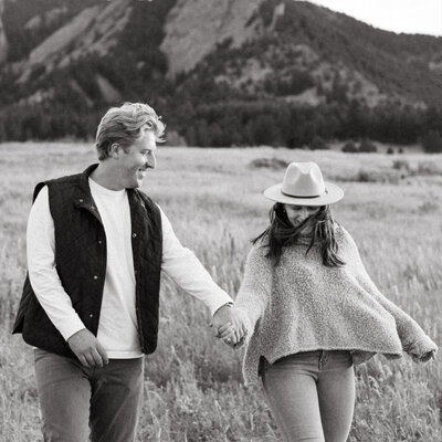 The couple walk hand in hand at the base of the mountains in Boulder, Colorado for their engagement session. The foothills at the base of the mountains are the most beautiful shade of green.