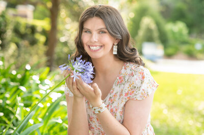 High school senior girl holding purple flowers while smiling at the camera.