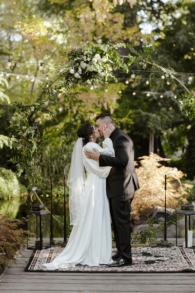 bride and groom kissing in front of a circle arch covered in greenery