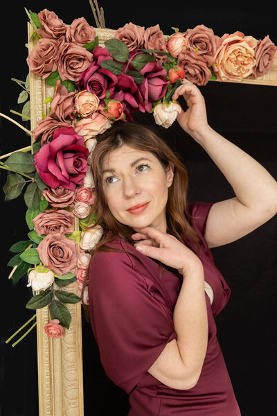 A woman leaning against a large picture frame with flowers