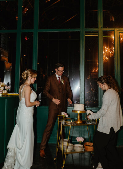 Behind-the-scenes moment of cake setup at The Little Chapel at Haven Ridge with bride and groom observing in anticipation.