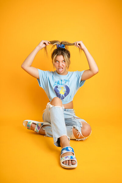 teen on yellow backdrop pulling ponytail and making funny face