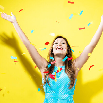 Woman who is excited with her arms outstretched standing against a yellow background