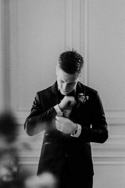 Groom gets ready  by adjusting his cufflinks in black and white photo