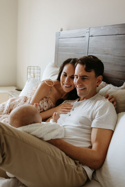 parents with newborn baby sitting in bed