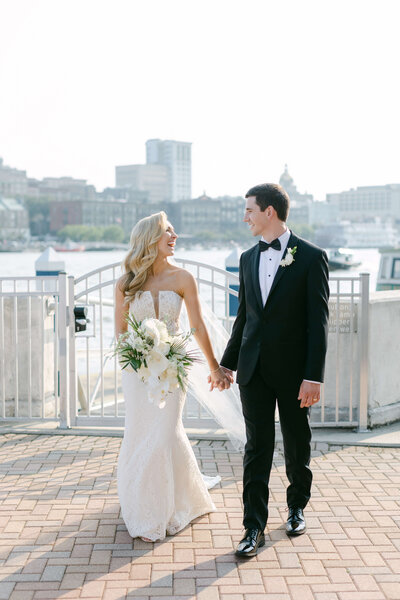A bride and groom hold hands on the dock of the Westin Savannah