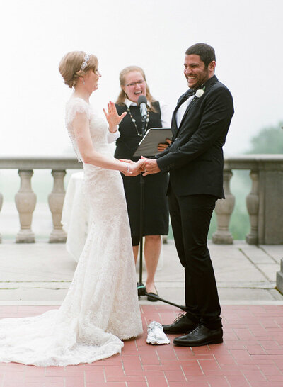 Reverend Pat Werk officiates a wedding ceremony as the bride and groom hold hands and laugh