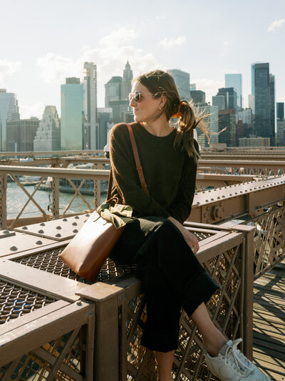 Bailee sitting on a railing and looking off to the side with a city skyline in the background