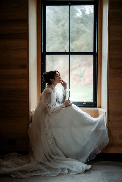 Bride in victorian dress sitting on a window seal and finishing writing her vows in Scotland