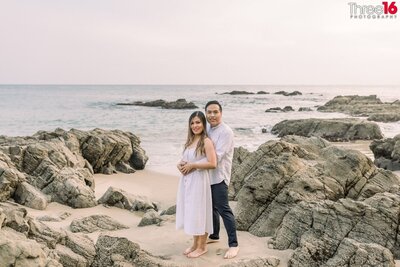 Bride to be leans back and kisses her Groom while standing amongst the rocks on the Crescent Bay Beach in Laguna Beach